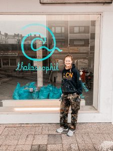 Inhaberin Elisabeth Wagener steht vor dem Schaufenster ihres Unverpacktladens in Wilhelmshaven. Neben ihr ist ihr Schaufensterlogo in blauer Farbe.