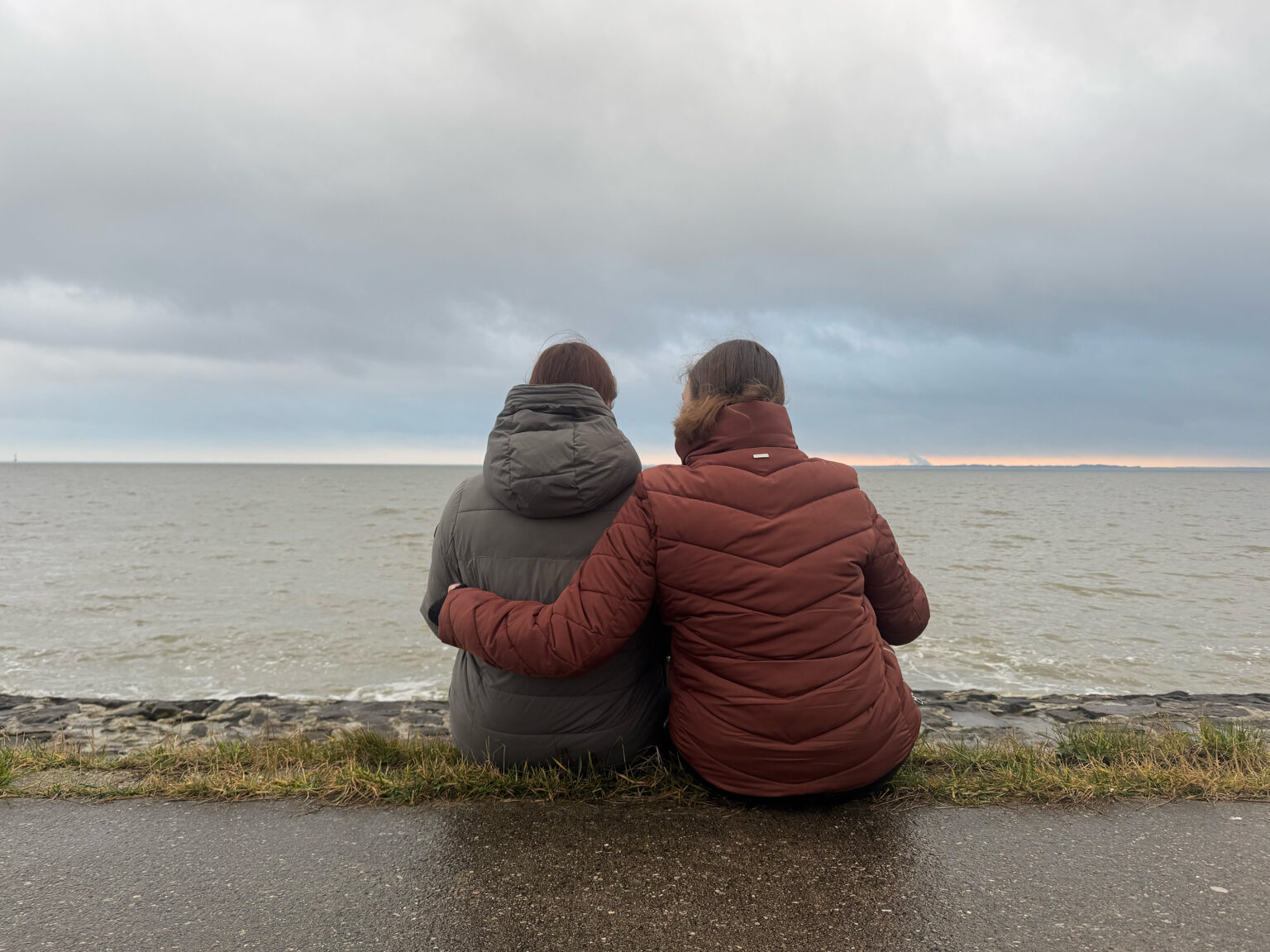 Von links: Autorinnen Pia und Britta sitzen vor dem Wattenmeer. Sie haben sich im Arm.