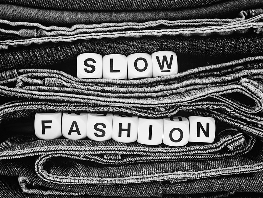 Viele Jeans und auf den Jeans wird "Slow Fashion" in Würfeln gelegt dargestellt