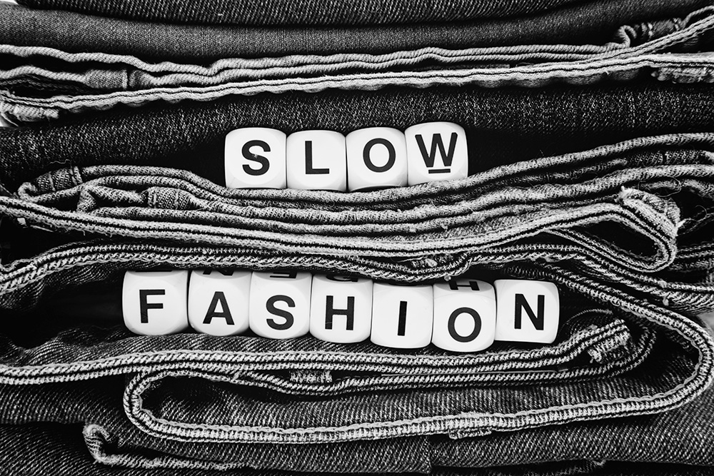 Viele Jeans und auf den Jeans wird "Slow Fashion" in Würfeln gelegt dargestellt