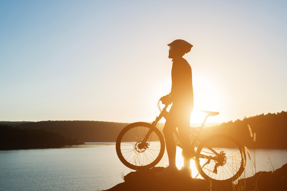 Mann steht im Sonnenuntergang mit seinem Fahrrad. Er trägt einen Helm und schaut links. Designed by Freepik.