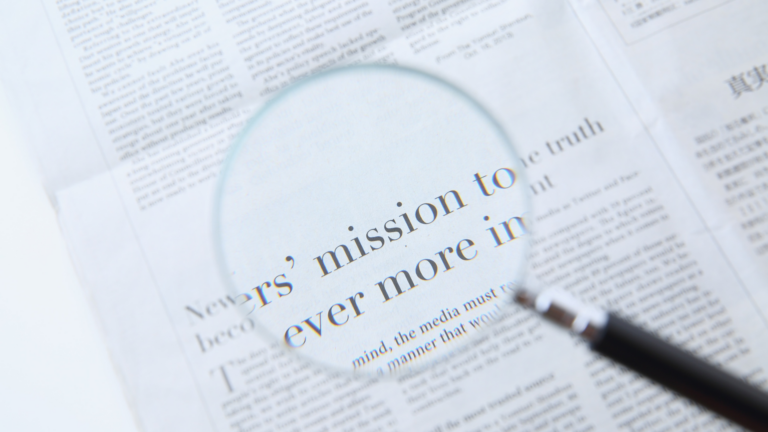 Lupe zoomt auf einen Zeitungsartikel. Quelle: Canva Premium https://www.canva.com/photos/MAGcvjyFKXw-close-up-of-newspaper-text-under-magnifying-glass/