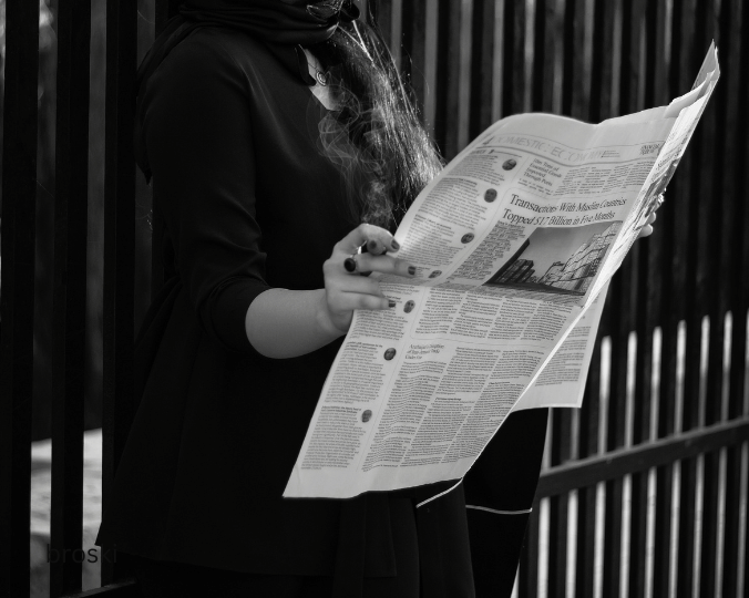 Ein schwarz-weiß Bild einer Person, die stehend eine aufgeschlagene Zeitung liest. Quelle: Premium Canva https://www.canva.com/photos/MAEthTxCkKg-black-and-white-photo-of-a-woman-holding-newspaper/