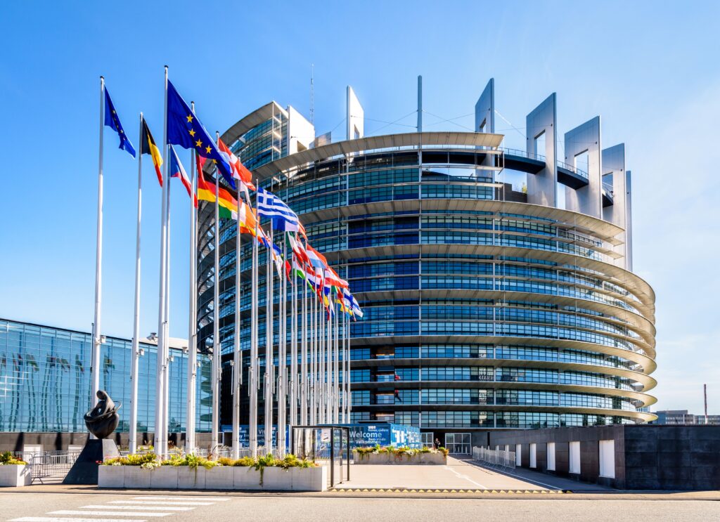 Ansicht des Gebäudes des Europäischen Parlamentes. Glasfassade mit im Wind wehenden europäischen Fahnen.