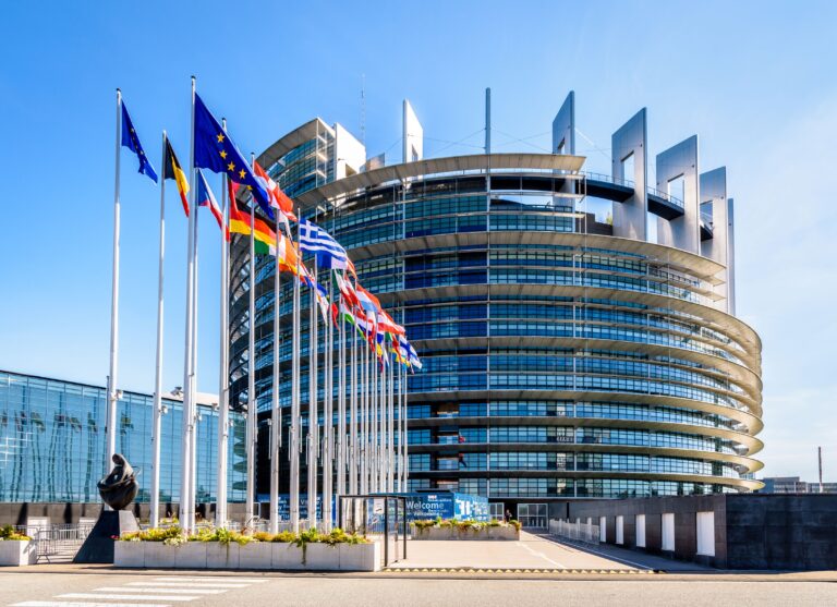 Ansicht des Gebäudes des Europäischen Parlamentes. Glasfassade mit im Wind wehenden europäischen Fahnen.