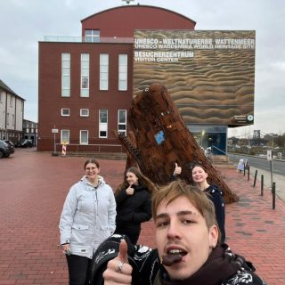 Vorne: Tom mit Lebkuchen im Mund. Von hinten links: Svea, Britta und Pia vor einer Walstatue. Kulisse am Wattenmeerbesucherzentrum Wilhelmshaven.